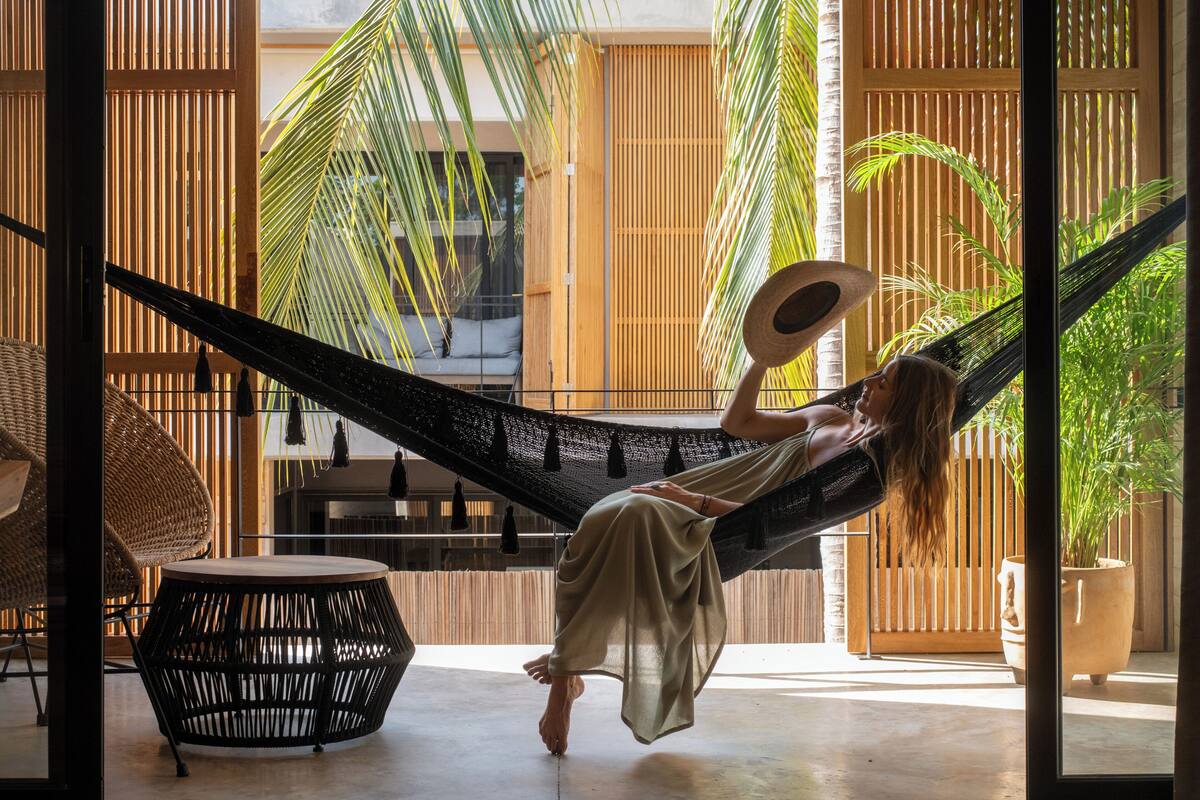 A person relaxing in a hammock in a room with a view of palm trees and bamboo partitions.