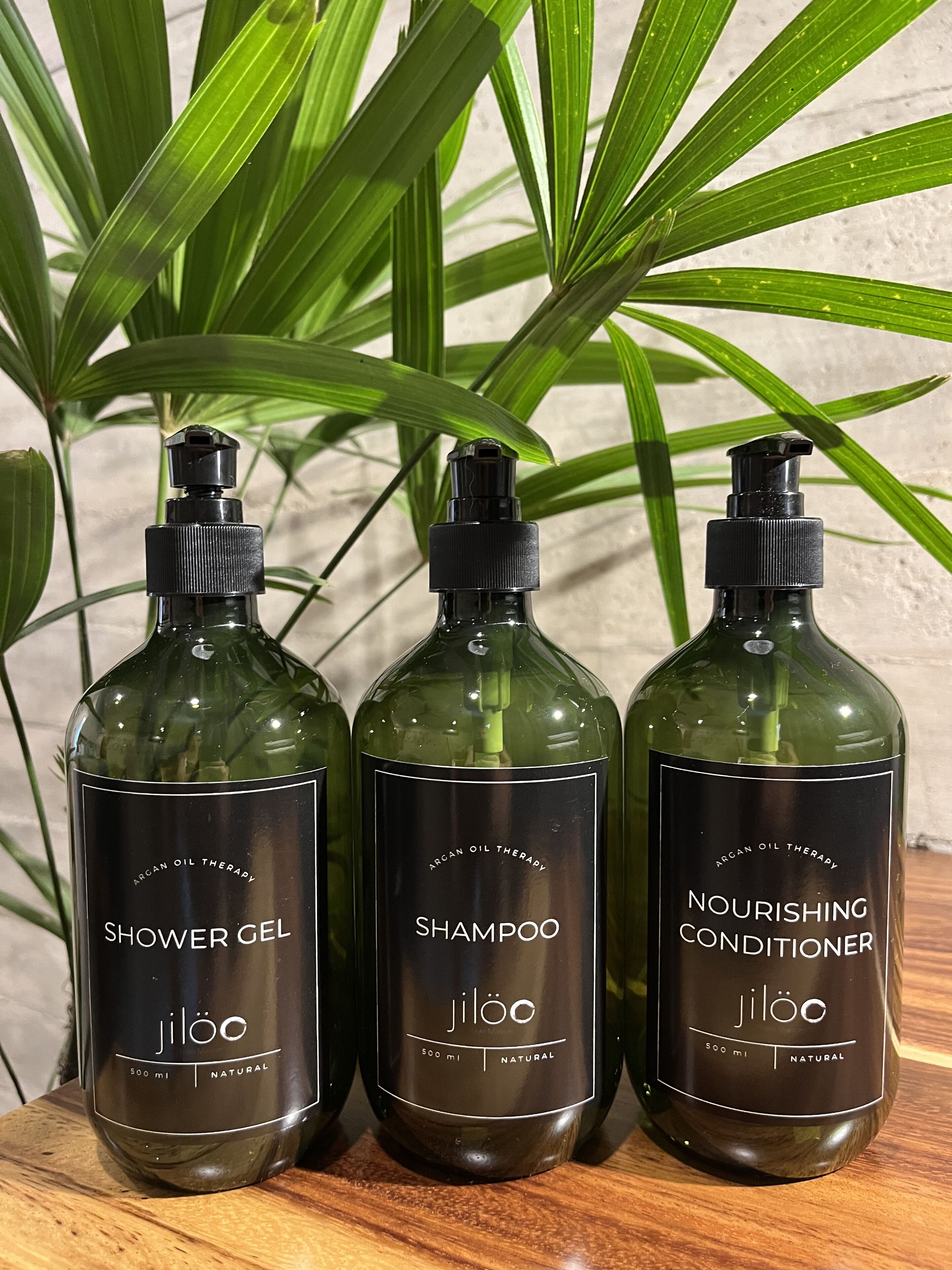 Trois flacons de produits Jiloo : un gel douche, un shampooing et un après-shampooing nourrissant, chacun portant la mention « 500 ml » et « produit naturel ».