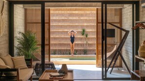 A modern living room with a sofa, coffee table, and a view of a wooden wall and a pool. - Hotel JILOO Petite Maison (Santa Maria Colotepec)
