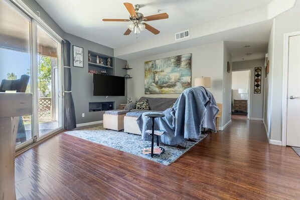 A modern living room with a flat-screen TV, a ceiling fan, and a large abstract painting.