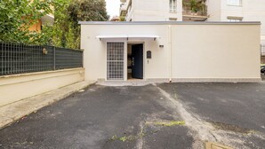 A gated parking area with a small building entrance, a paved road, and a fence.
