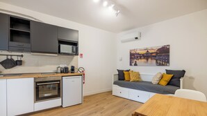 A compact kitchen with a microwave, oven, and sink. A dining table and a sofa with cushions are also visible.