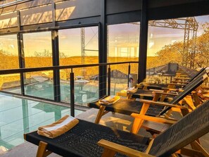 Zona de relax iluminada por el sol con sillones y suelo de cristal, con vistas a una zona en construcción.
