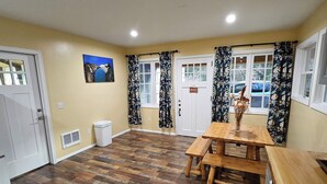 A spacious room with a wooden dining table and benches, a white door, and a window with floral curtains. - Charming barn loft in quaint Marshall (Marshall)