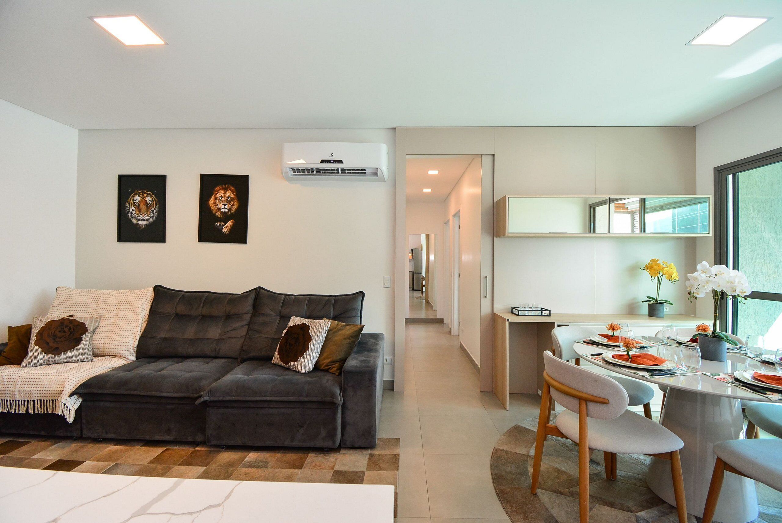 Ein modernes Wohnzimmer mit einem dunkelgrauen Sofa, zwei gerahmten Kunstwerken und einem Essbereich mit rundem Tisch und Stühlen.
