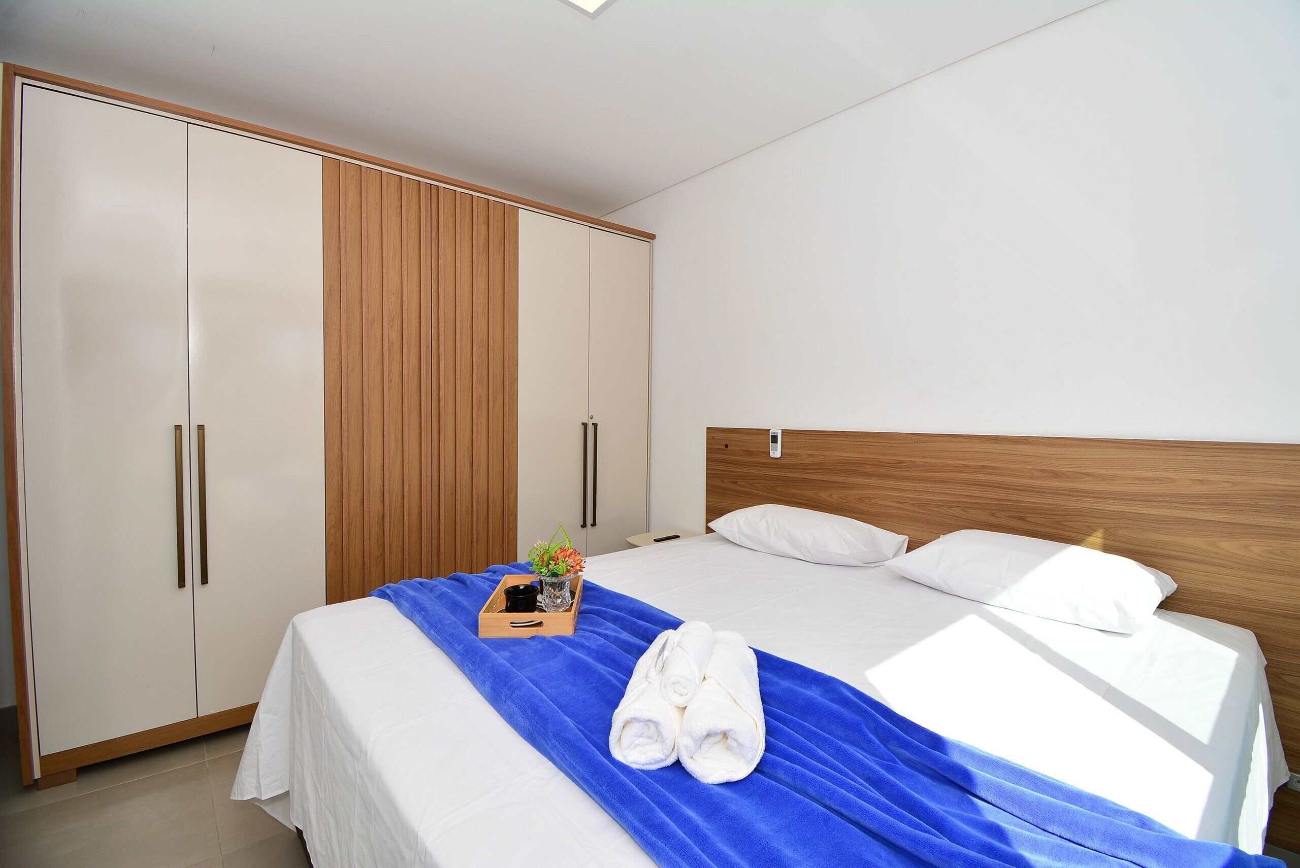 A hotel room with a bed, a wooden wardrobe, and a small table with a vase and towels.
