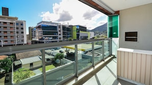 A balcony with a glass railing overlooking a parking area and buildings. - Floripa Residence-Apartamento 3 quartos (Florianopolis)