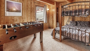 A cozy room with wooden walls, a futon bed, a foosball table, and a framed picture of lightning on the wall. - Forest Edge Retreat (Big Bear City)