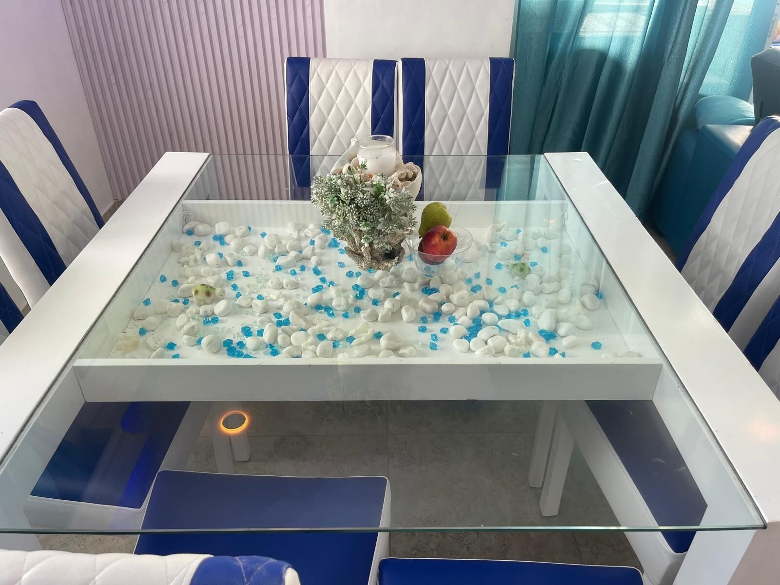 A glass-top dining table with a decorative centerpiece and blue and white striped chairs.