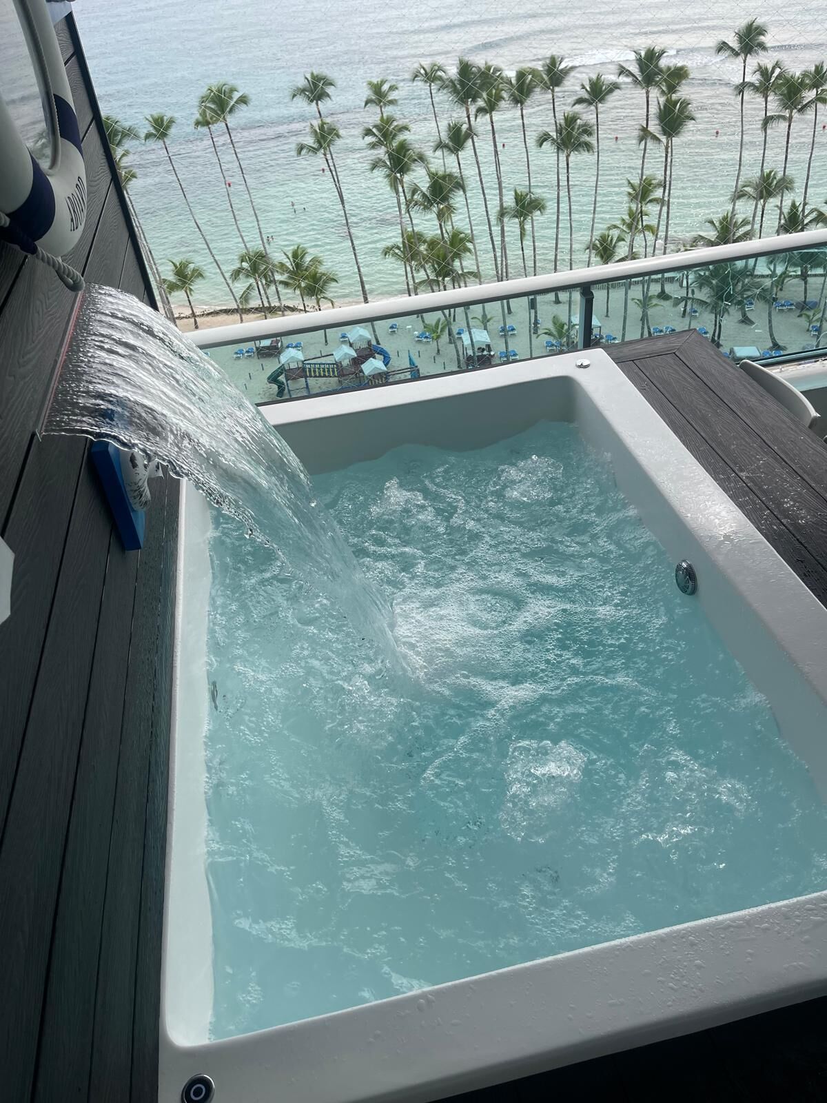 Een whirlpool met waterval, met uitzicht op een strand met palmbomen en een zwembad.