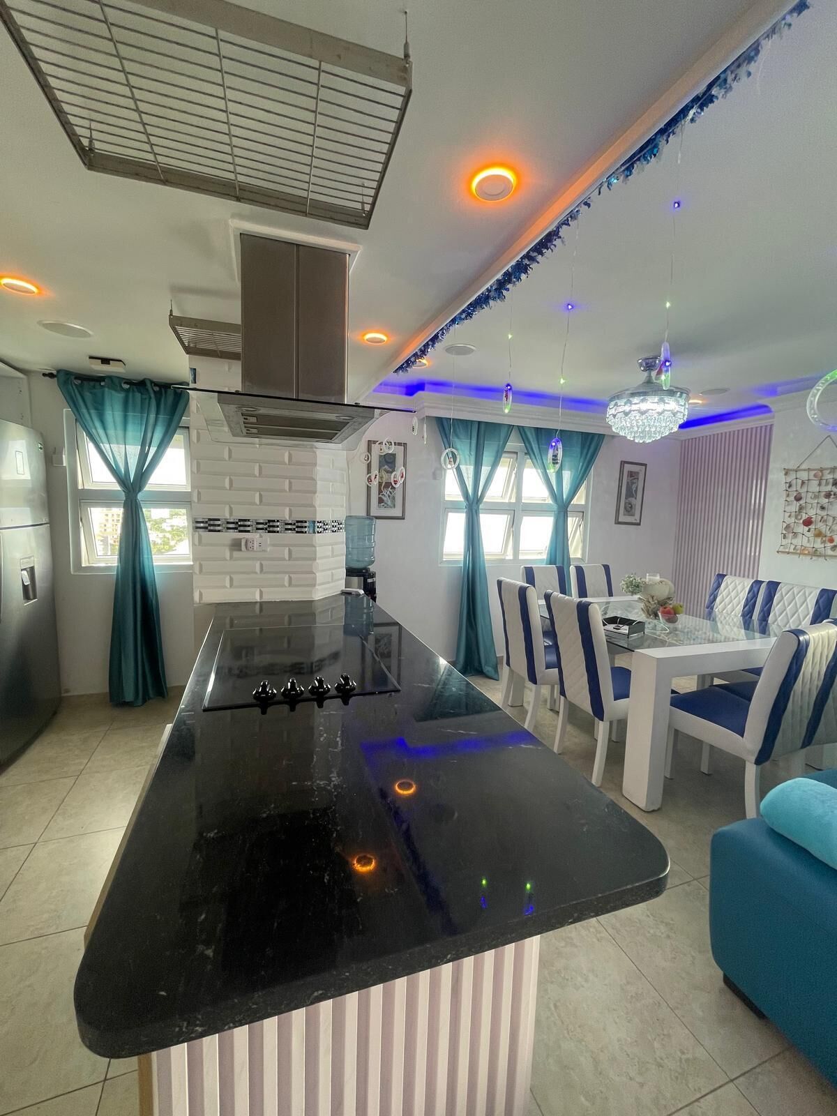 A modern kitchen with a black countertop, white cabinets, and a dining area with blue and white chairs.