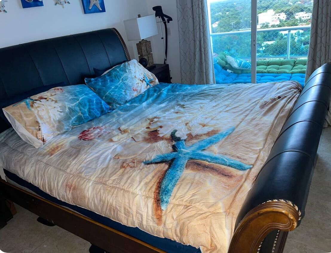 A bed with a starfish design, a black headboard, and a view of greenery outside.