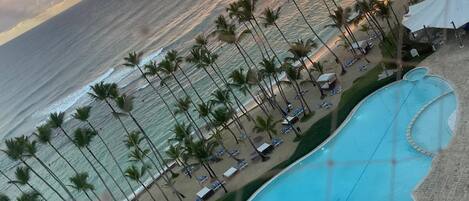 A beach resort with a swimming pool, palm trees, and a sunset view.