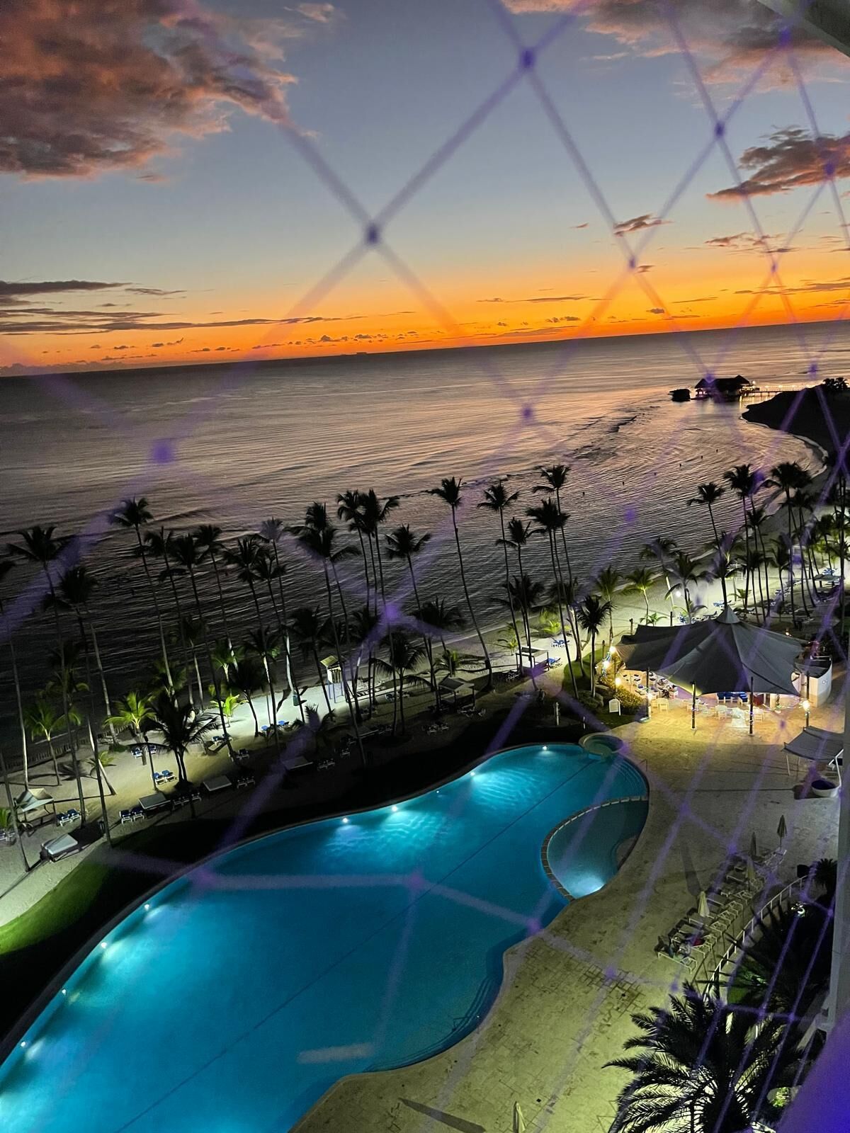 Un complexe hôtelier doté d’une piscine, de palmiers et offrant une vue sur l’océan au coucher du soleil.