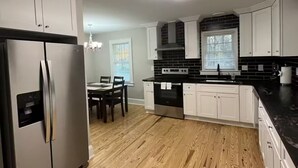 Une cuisine moderne avec des meubles blancs, un réfrigérateur en acier inoxydable, un plan de travail noir et un plancher en bois.