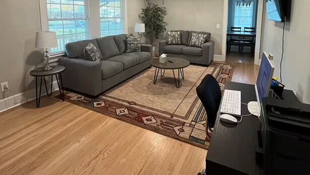 Un salon spacieux avec un canapé gris, une table basse et un bureau avec un ordinateur.