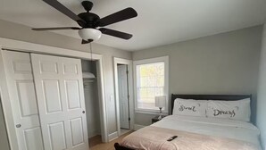 Une chambre à coucher avec un lit, un ventilateur de plafond, une fenêtre et une porte.