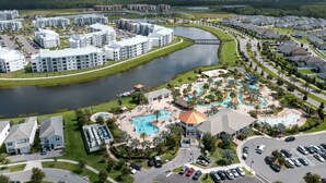 An aerial view of a residential area with apartment buildings, a swimming pool, and a bridge over a water body. - Storey Lake 4 BR With Private Pool (Kissimmee)