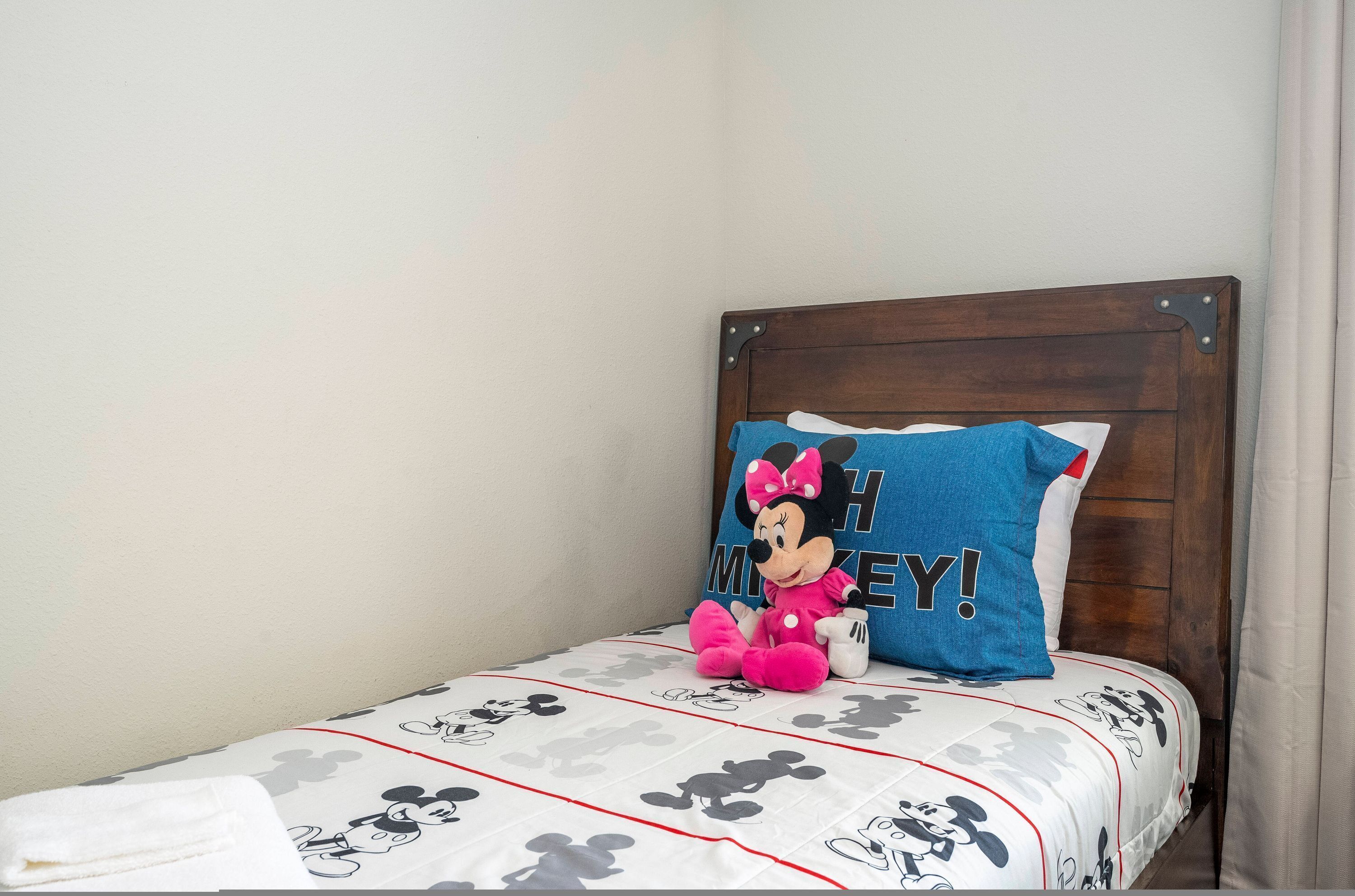 Ein Einzelbett mit Bettdecke und Kopfkissen im Mickey Mouse Design, sowie einer Mickey Mouse Kuscheltierfigur.