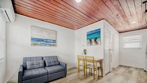 Une pièce avec un canapé gris, une table à manger en bois avec des chaises, une porte blanche et un plafond avec des poutres en bois.