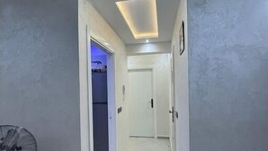Corredor com ventilador de teto, luminária embutida e porta que dá para outro quarto.