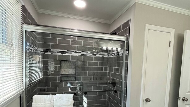 Une douche à l’italienne avec une porte en verre, des murs carrelés et un sol gris.