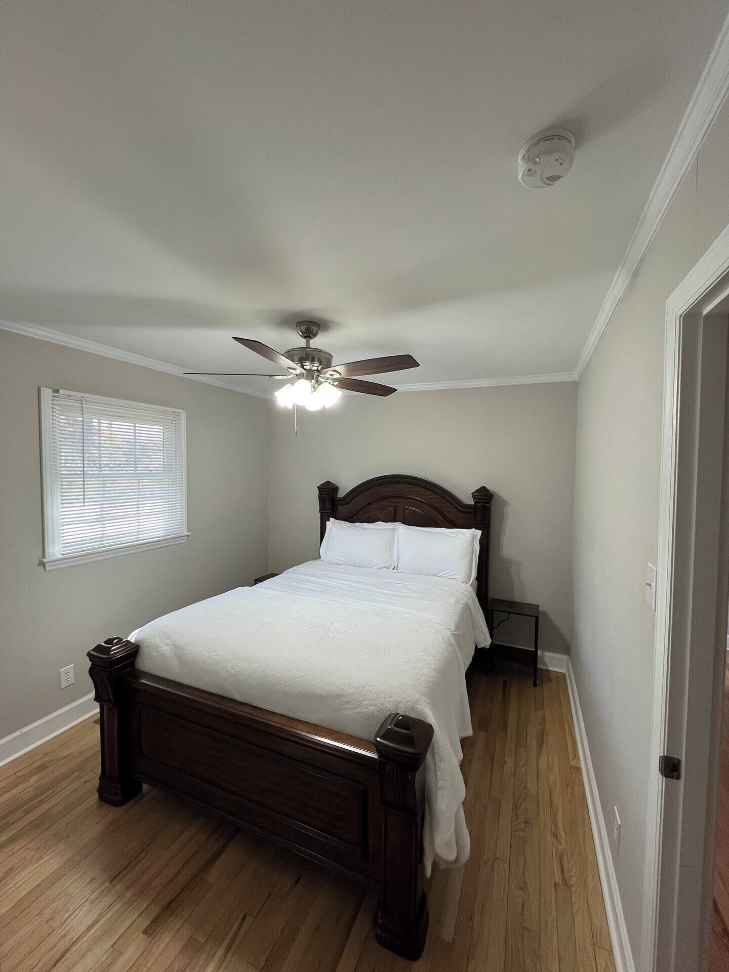 Un dormitorio con cama de madera, ventilador de techo, mesita de noche y ventana con persianas.