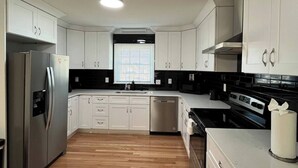 Une cuisine moderne avec des armoires blanches, des appareils en acier inoxydable et un plancher en bois.