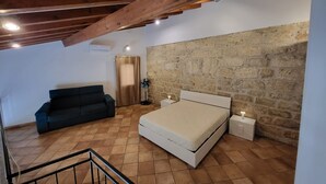 Ein Schlafzimmer mit Steinwand, einem Bett, einem Nachttisch, einem Ventilator, einem Fenster mit Vorhang und einer Treppe.