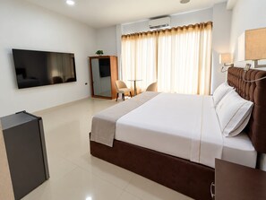 A hotel room with a bed, a TV, a desk, a chair, a wardrobe, and a window with curtains. - Hotel Embassy Suites (Nauta)