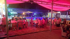 An outdoor dining area with tables and chairs, a pool, and a covered seating area. - Hotel Embassy Suites (Nauta)