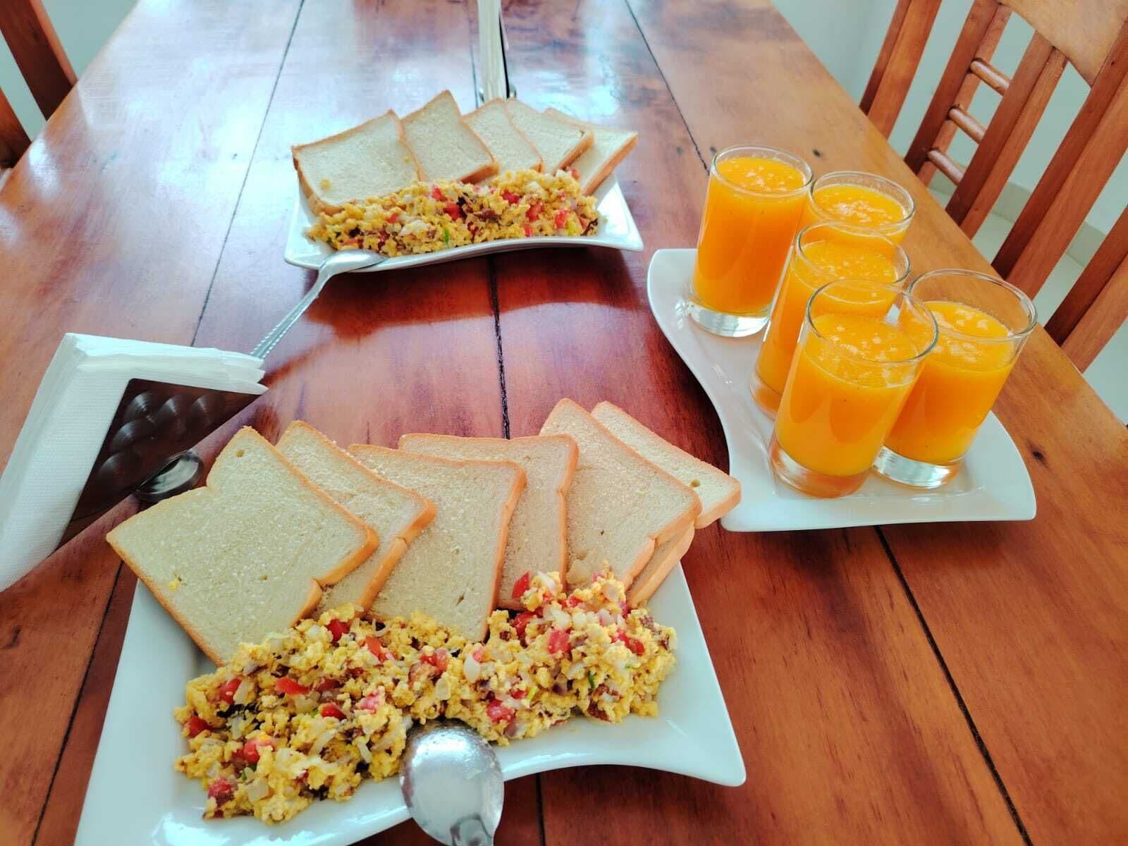 Una mesa de madera con platos de huevos revueltos, tostadas y vasos de jugo de naranja.