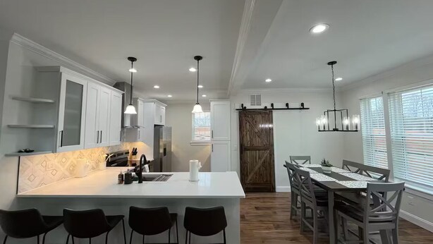 A modern kitchen with white cabinets, a central island with bar stools, and a dining area with a wooden table and chairs. - Cozy Jersey (Haw River)