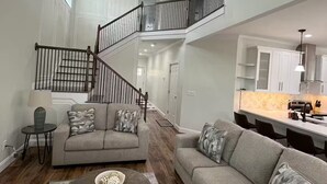 A spacious living area with a high ceiling, a staircase, and a kitchen area. - Cozy Jersey (Haw River)