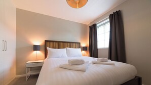 Ein ordentlich bezogenes Bett mit weißen Leinen und Handtüchern, ein Nachttisch mit einer Lampe und ein Fenster mit Vorhängen.