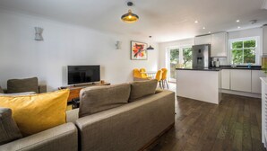 Ein modernes Wohnzimmer mit Sofa, Fernseher und Essbereich mit gelben Stühlen.