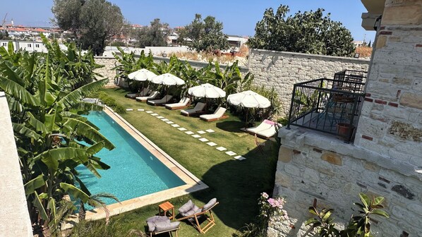 A pool with lounge chairs and umbrellas, surrounded by greenery and a stone wall. - Elia Hotel Alaçatı (Cesme)