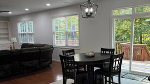 A dining area with a round table and chairs, a ceiling light fixture, and large windows with blinds.