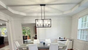 A dining area with a glass table, white chairs, and a chandelier.