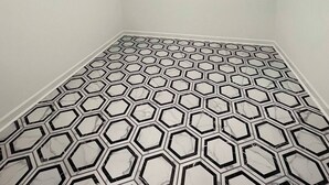 A room with a geometric patterned floor, a ceiling with two recessed lights, and a metal rack along the wall.