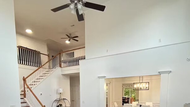 A spacious living room with a brown leather armchair, a dark coffee table, and a gray sofa. A staircase with wooden railings leads to an upper level.