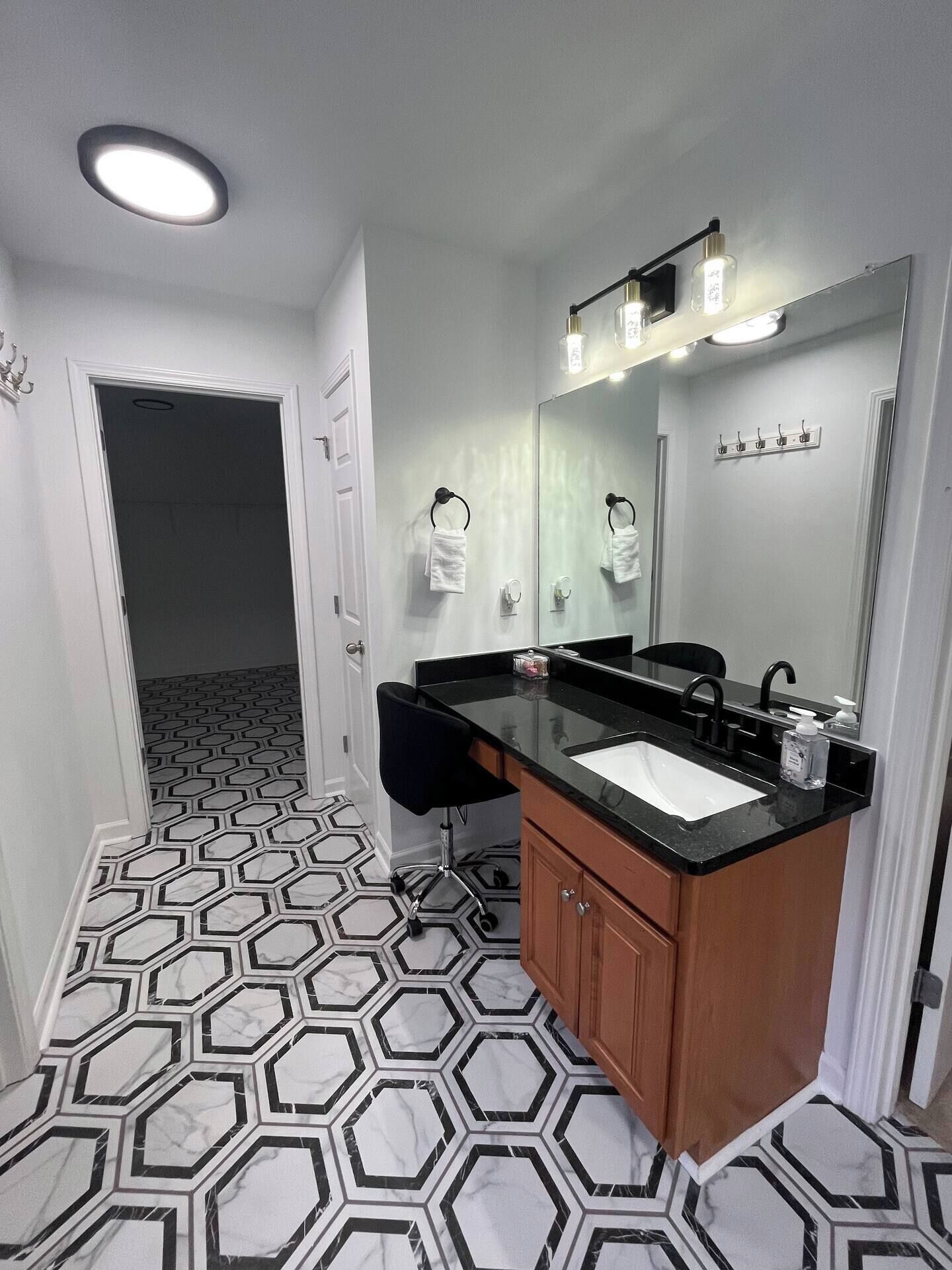 A bathroom with a black countertop sink, a large mirror, and a hexagonal patterned floor.