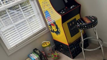 A room with a Pac-Man arcade machine, a window with blinds, and various toys on the floor.