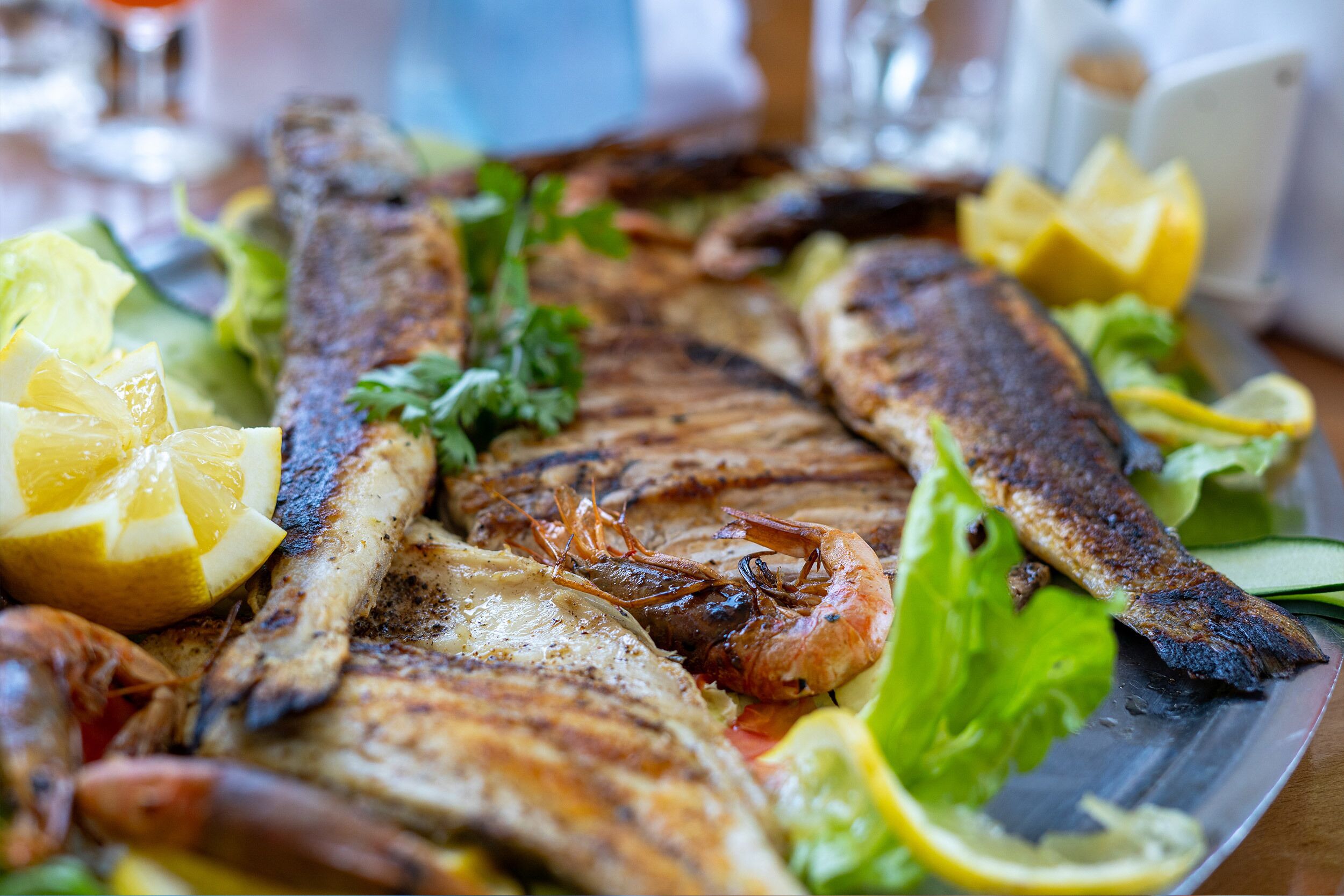 Una bandeja de mariscos con pescado a la parrilla, camarones y rodajas de limón.