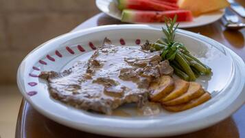 Un plato de comida con carne y verduras, una guarnición de pan en rodajas y hierbas frescas.
