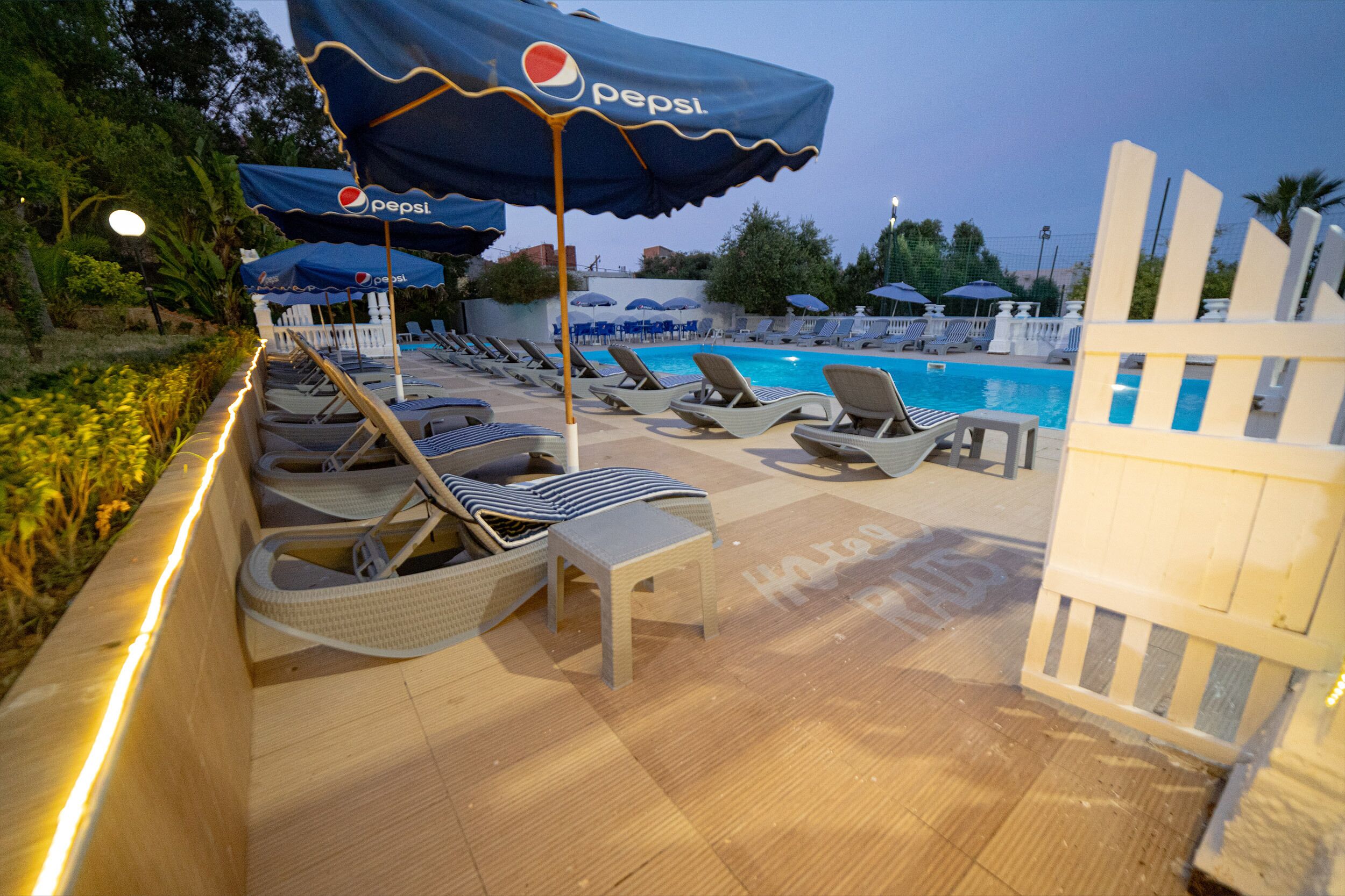A poolside area with lounge chairs and umbrellas, some with Pepsi branding.