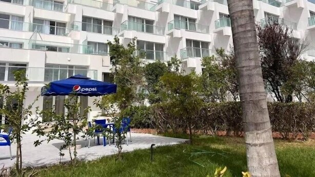 A modern building with multiple balconies and a garden area with chairs and a Pepsi-branded umbrella. - Rais El Marsa (Algiers)