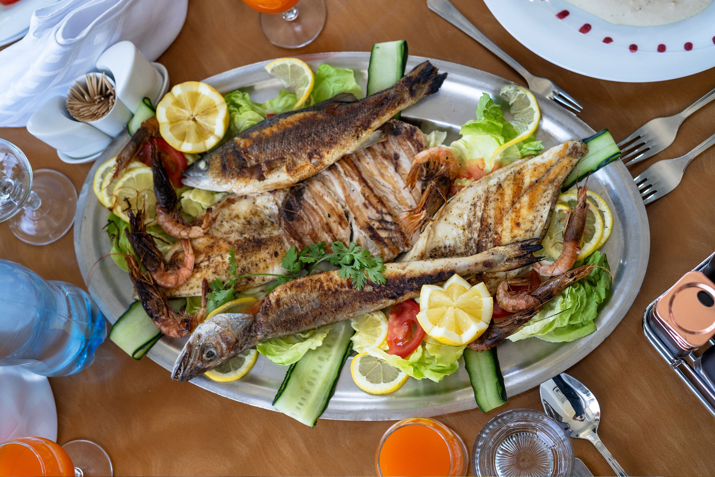 A meal with grilled fish and shrimp on a bed of lettuce, lemon slices, and cucumber.