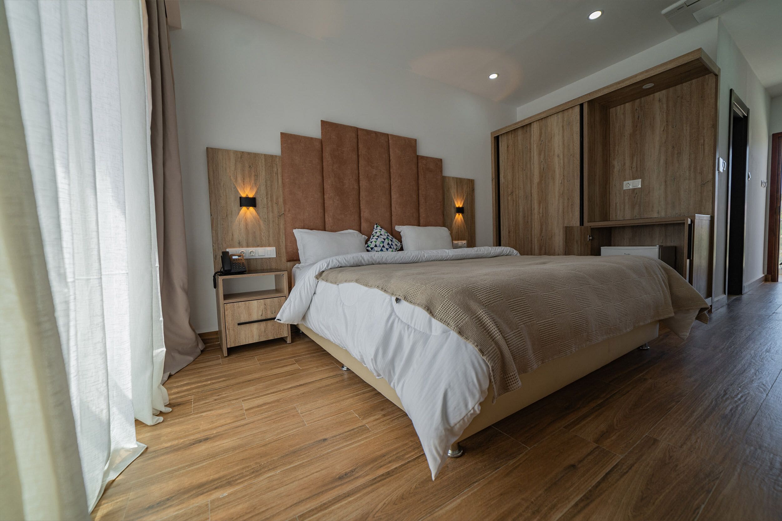 A modern bedroom with a large bed, wooden headboard, bedside tables, and built-in wardrobe.