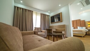 A hotel room with a sofa, armchair, a small table, a TV mounted on the wall, and a bed with a headboard. - Rais El Marsa (Algiers)